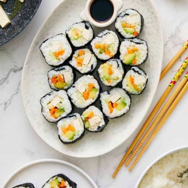Fresh vegetable sushi rolls with soy sauce on a marble surface, featuring colorful fillings like carrots, cucumbers, and avocados, perfect for healthy eating.