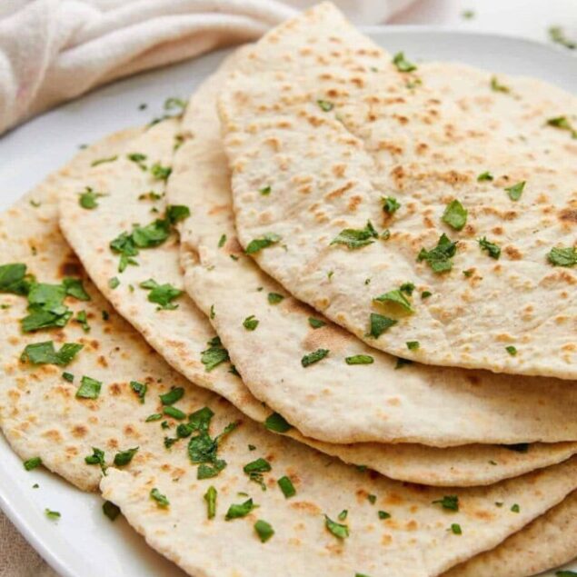 Flour tortillas garnished with chopped fresh cilantro on a white plate.