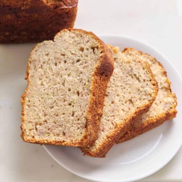 Moist banana bread slices on white plate with whole loaf in background, healthy baking, easy banana bread recipe, homemade bread, gluten-free baking options.