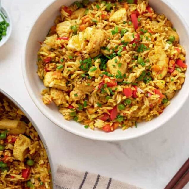 Savory chicken fried rice with vegetables in a white bowl, garnished with chopped green onions and parsley. Perfect healthy meal idea for weeknights or meal prep.