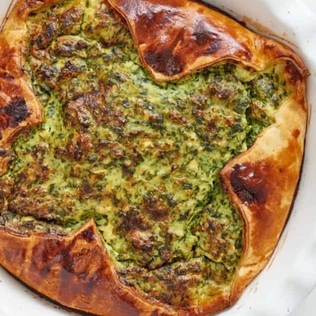 Savory spinach and cheese stuffed pastry with golden brown crust, baked to perfection in a white baking dish.