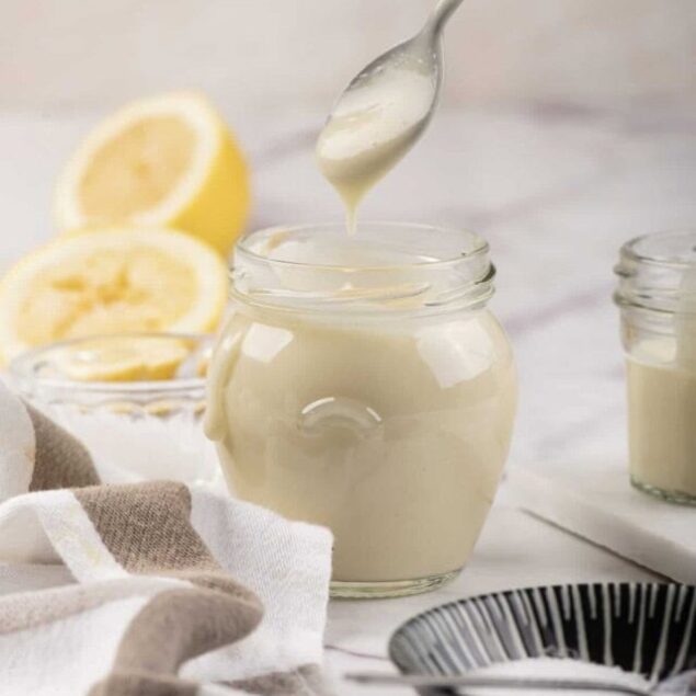 Creamy homemade lemon yogurt in a glass jar with fresh lemon slices in the background, perfect for healthy eating and nutritious recipes. Ideal for dessert, breakfast, or snacks.