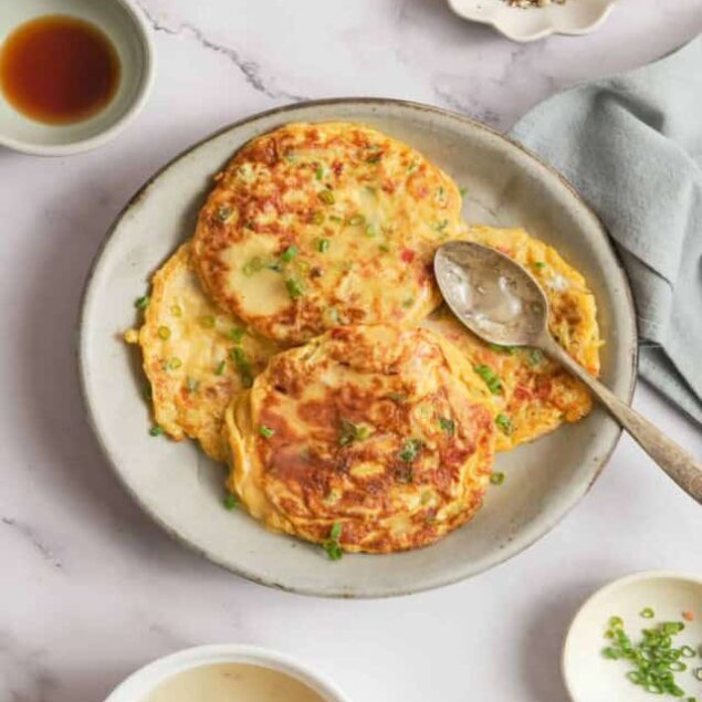 Fluffy vegetable pancakes garnished with green onions served on a white plate, accompanied by dipping sauces and salt, creating a delicious healthy breakfast or brunch option.