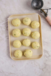 Potato balls scooped and formed on a parchment-lined tray.