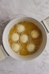 Potato balls frying in hot oil in a light-colored pot.