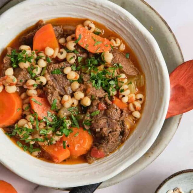 Hearty beef and vegetable stew with pearl barley, carrots, and fresh herbs in a rustic bowl for a nutritious, wholesome meal.