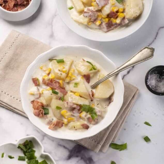 Creamy potato and bacon chowder with fresh green onions and corn, served in white bowls on a marble countertop. Perfect for comfort food lovers and easy to make at home.