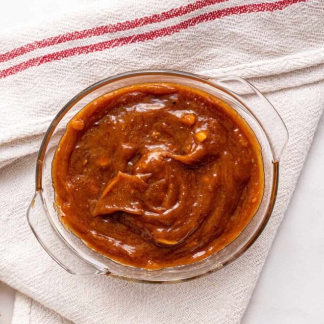Rich homemade barbecue sauce in a glass bowl on a white cloth napkin.