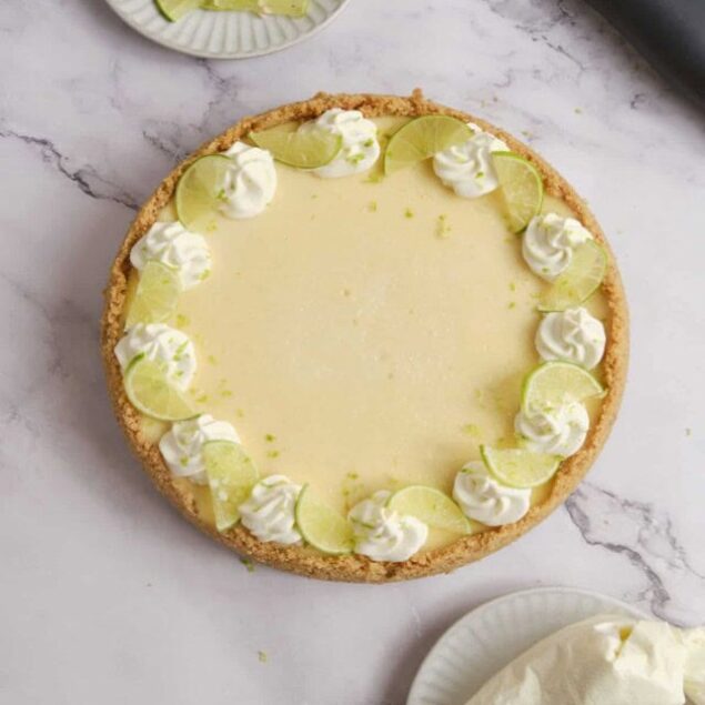 Lime pie on a marble surface with lime slices and whipped cream garnishes, perfect for a refreshing dessert.