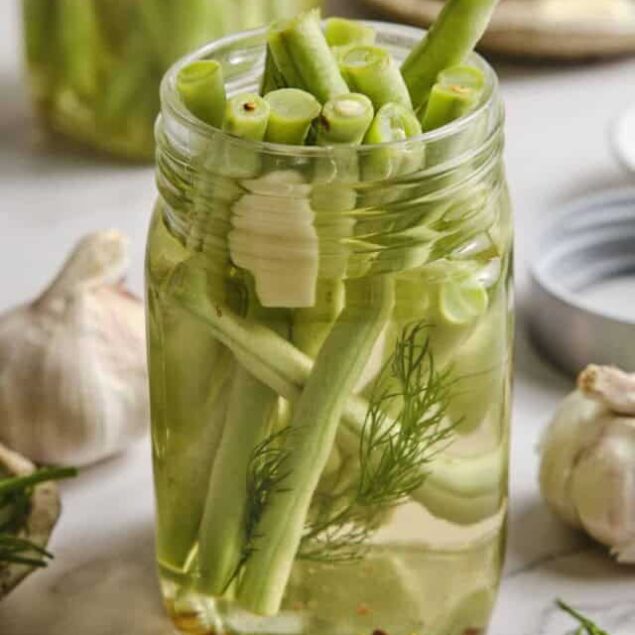 Sliced green garlic and fresh herbs in jar of infused water for detox or healthy drink.