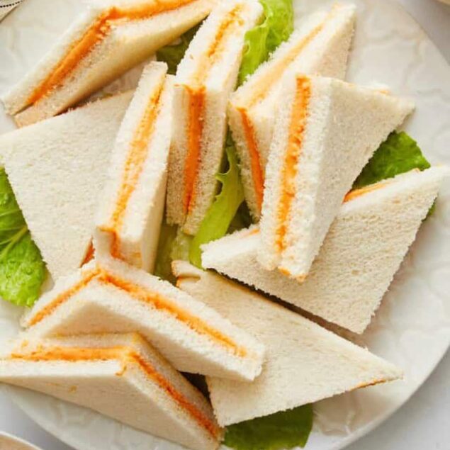 Cream cheese and carrot sandwich cut into triangles on a white plate with fresh lettuce, promoting healthy and delicious meal ideas.
