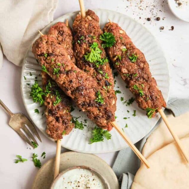 Juicy grilled beef kebabs garnished with fresh parsley on a white plate, served with creamy sauce and pita bread, perfect for healthy meals, high protein, and flavorful food options.
