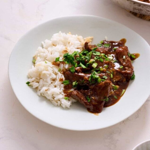 Savory beef stew served with fluffy white rice, garnished with chopped green onions, on a white plate for a healthy and comforting meal.