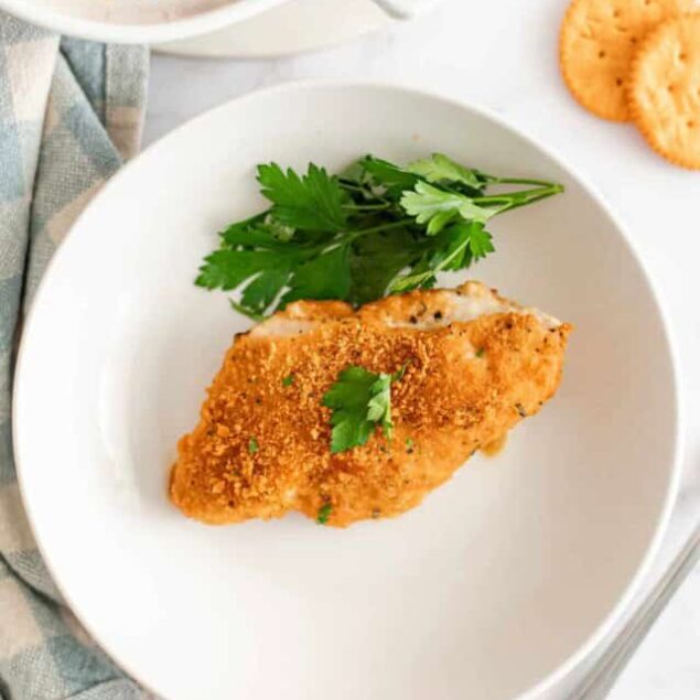 Juicy baked chicken breast with crispy coating and fresh parsley on a white plate, healthy and flavorful meal.