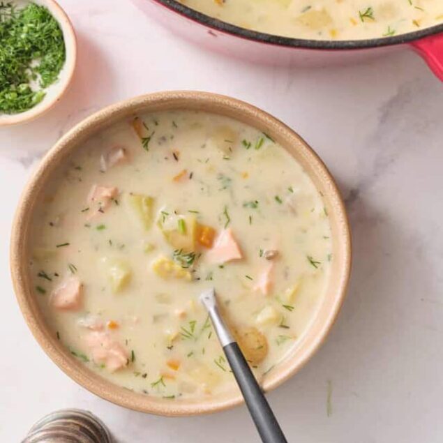 Creamy chicken and vegetable soup in a bowl, garnished with fresh herbs, on a white marble surface; comforting, healthy, easy chicken soup recipe, perfect for nutritious meals.