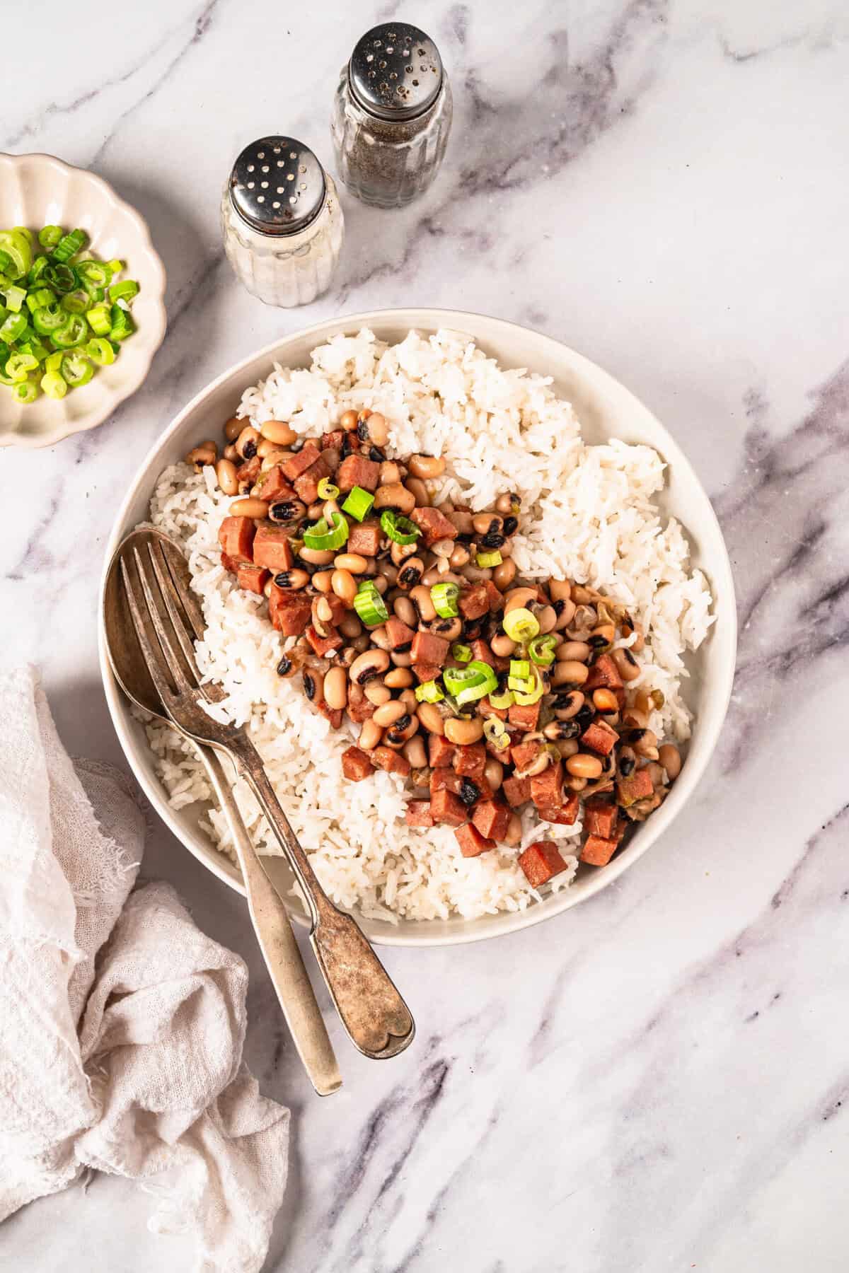 Savory black-eyed pea and rice bowl garnished with green onions on a white marble background, healthy vegan meal, food faith fitness, high-protein plant-based dish, easy nutritious recipe for weight loss.