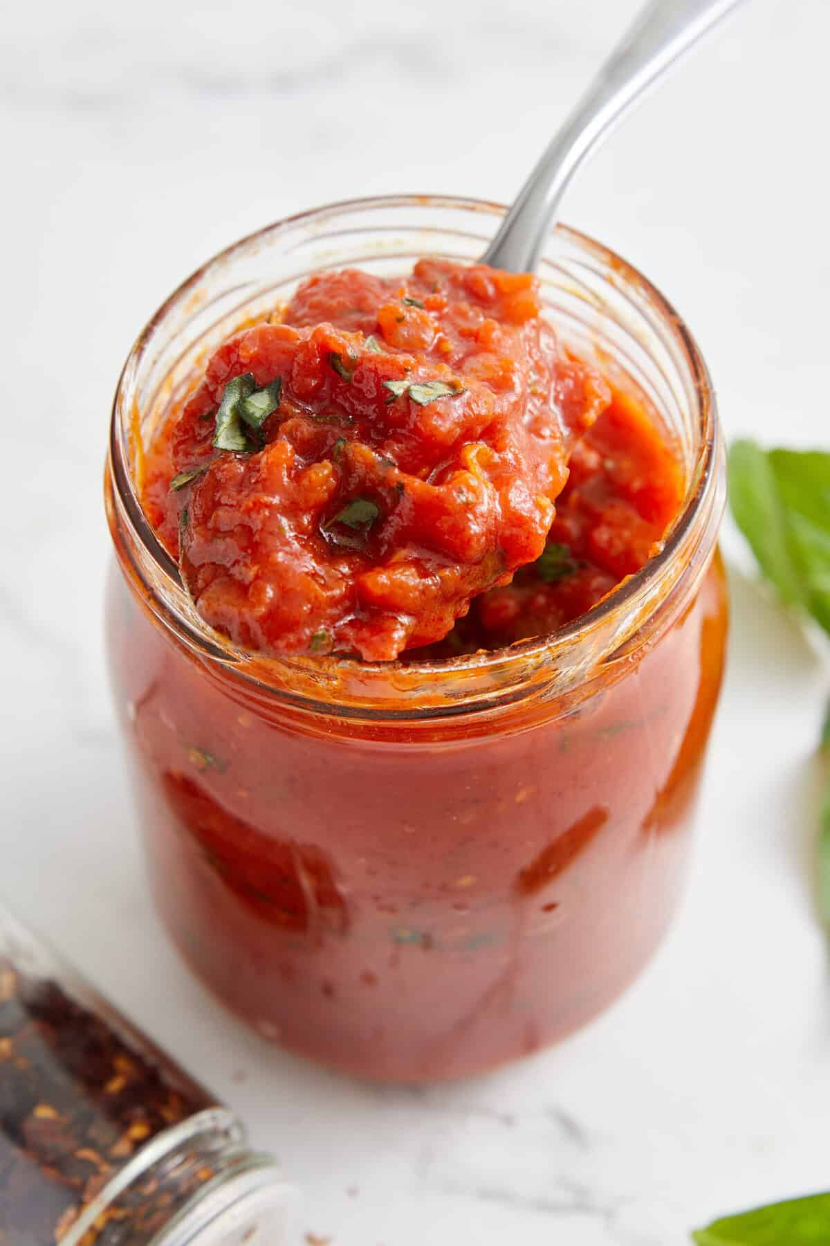 Savory homemade tomato sauce with fresh herbs in a glass jar, perfect for healthy recipes and meal prep.