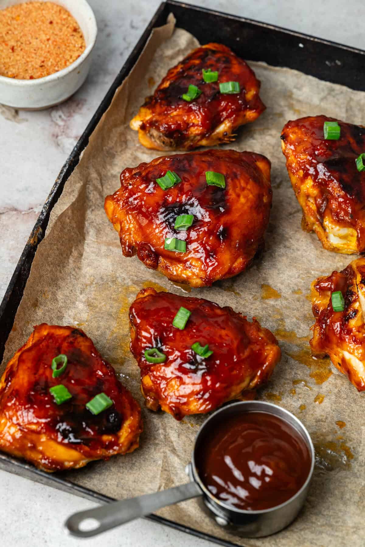 Juicy barbecue chicken drumsticks topped with chopped green onions on a baking sheet with a side of barbecue sauce, highlighting healthy meal prep, high-protein recipes, and flavorful chicken ideas for dinner or snacks.