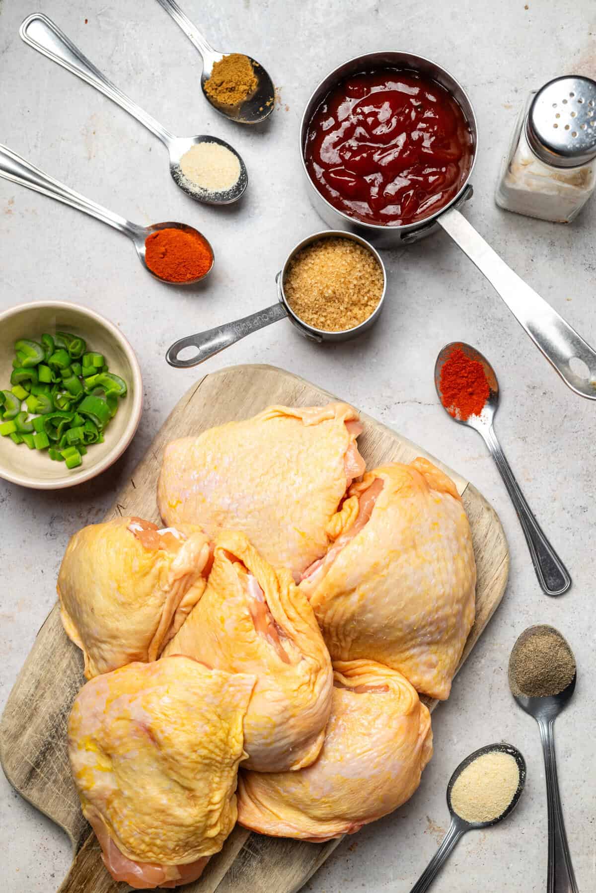 Juicy raw chicken thighs on a wooden cutting board surrounded by spices, green onions, and sauce ingredients for healthy meal prep or nutritious recipes.