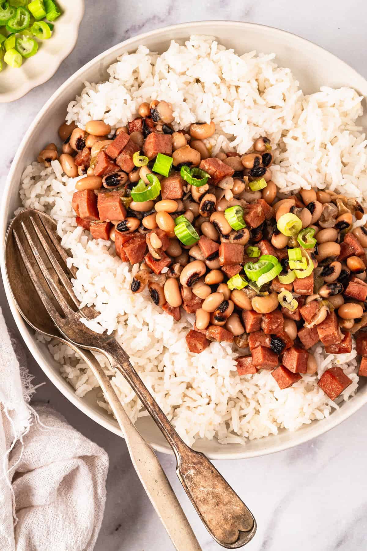 Savory vegan baked tuna casserole with rice, black beans, and diced vegan tuna, garnished with chopped green onions on a white bowl. Perfect healthy comfort food from Food Faith Fitness.