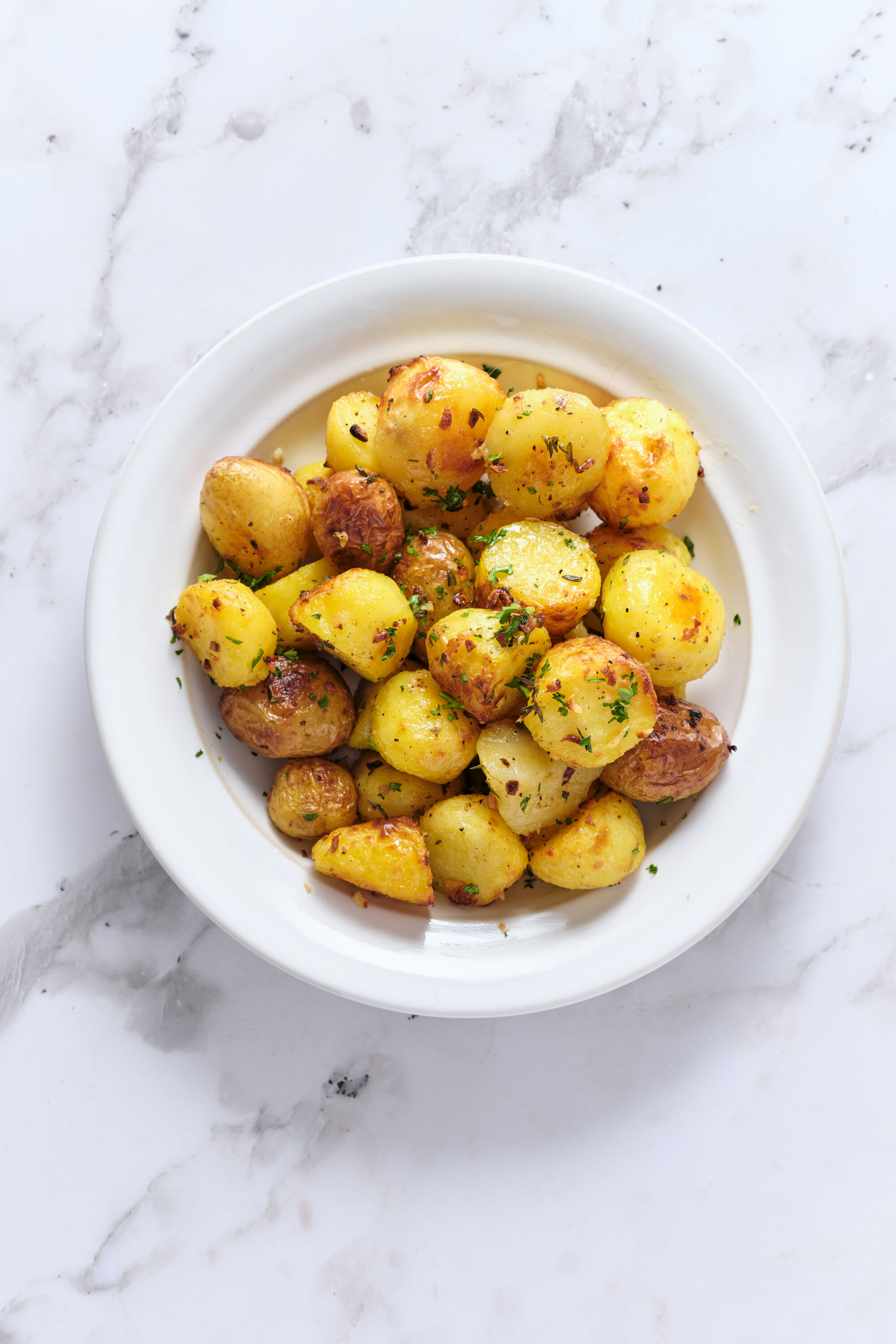 Golden roasted butter potatoes in a white bowl, garnished with fresh chopped herbs.