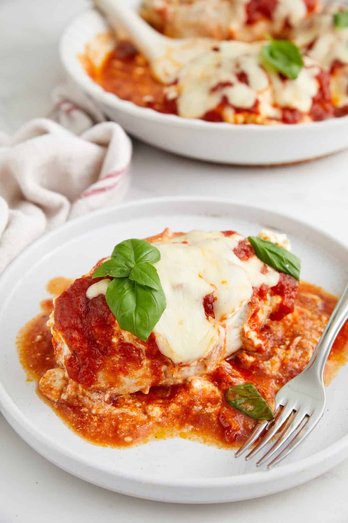 Savory baked eggplant parmesan with melted cheese, fresh basil, and tomato sauce, served on a white plate for a healthy and delicious Italian-inspired meal.