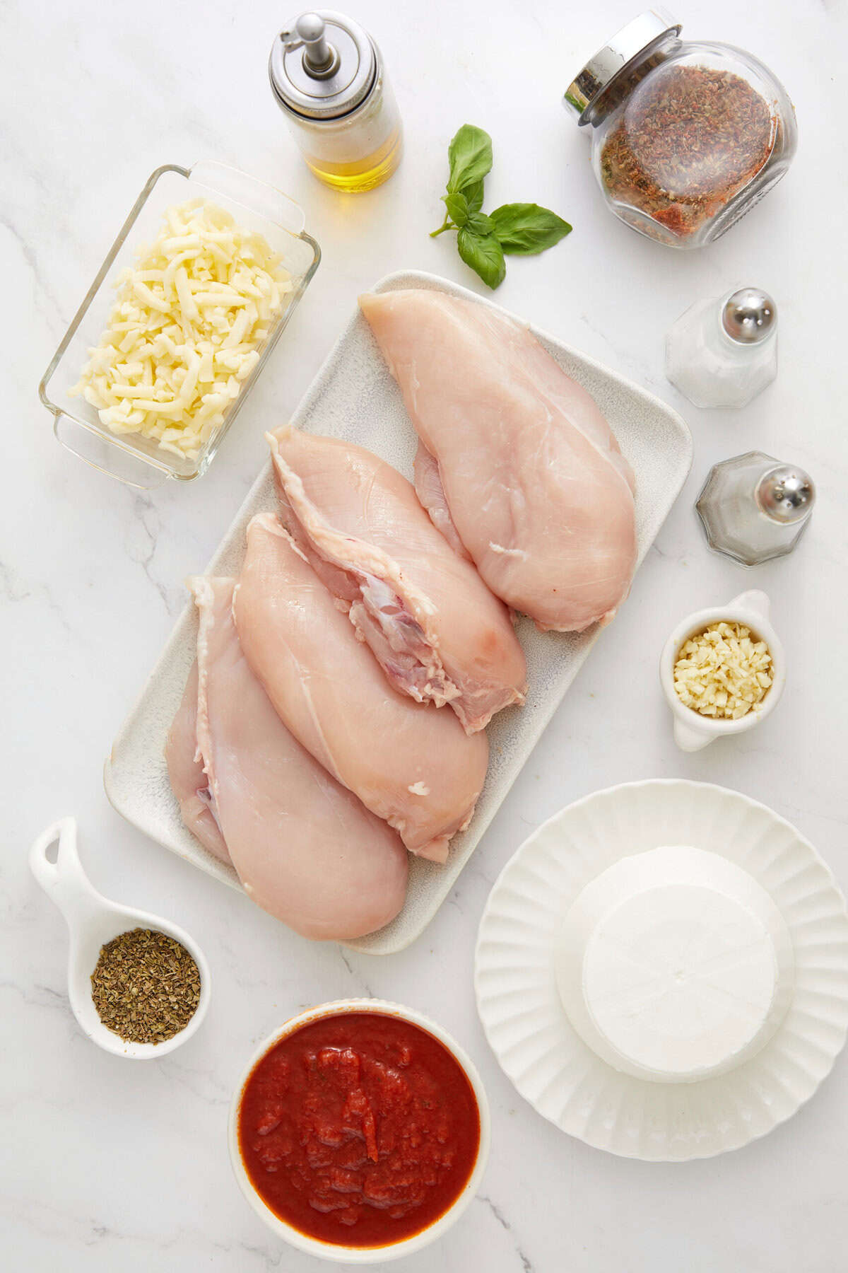 Juicy raw chicken breasts with herbs and spices, fresh garlic, and cooking ingredients on white marble surface for healthy meal prep.