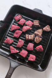 Garlic butter steak bites searing in a cast iron grill pan.