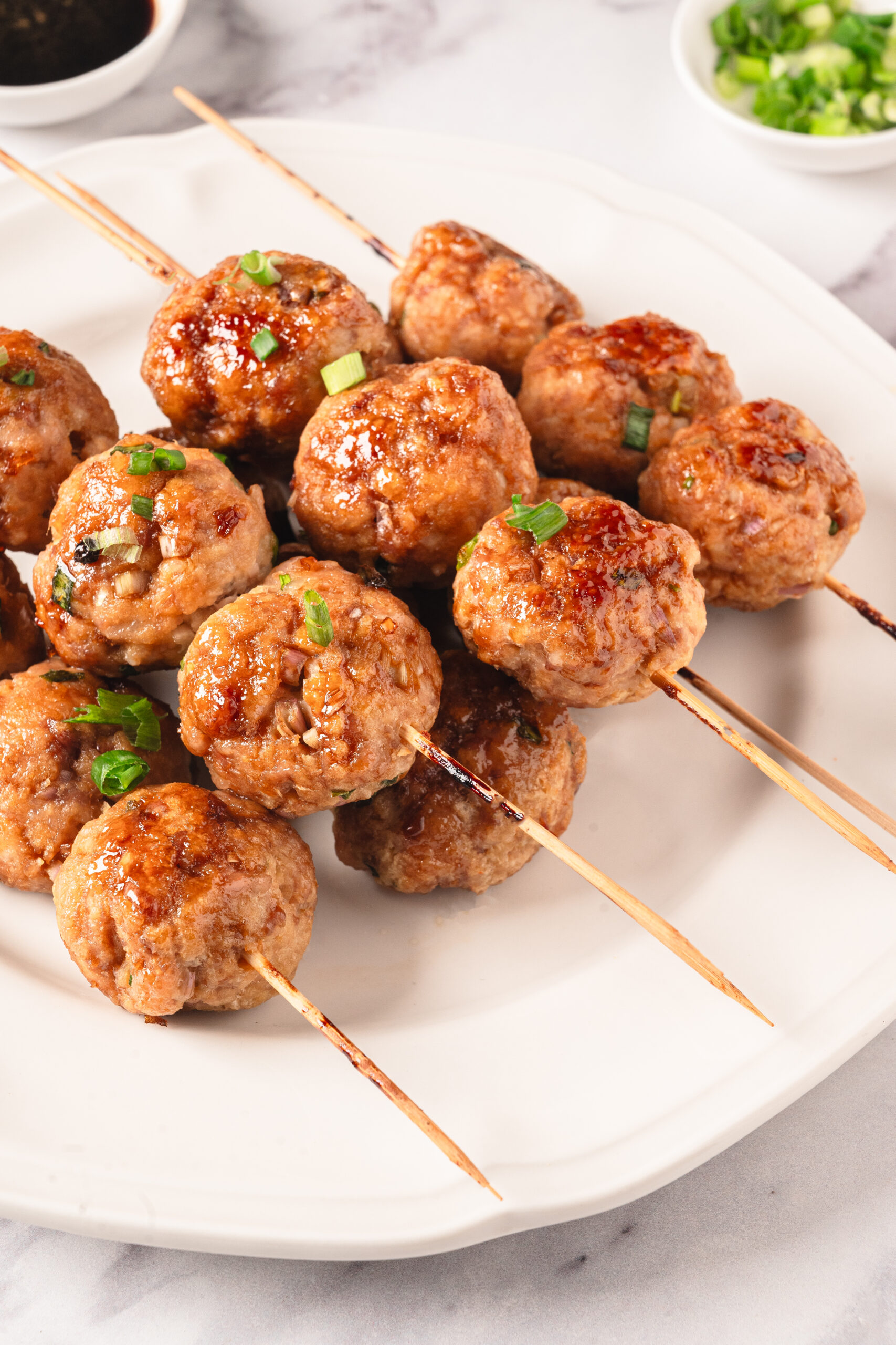 Juicy homemade meatballs on skewers with a savory glaze, garnished with green onions, served on a white plate. Perfect for healthy, high-protein meals and meal prep.