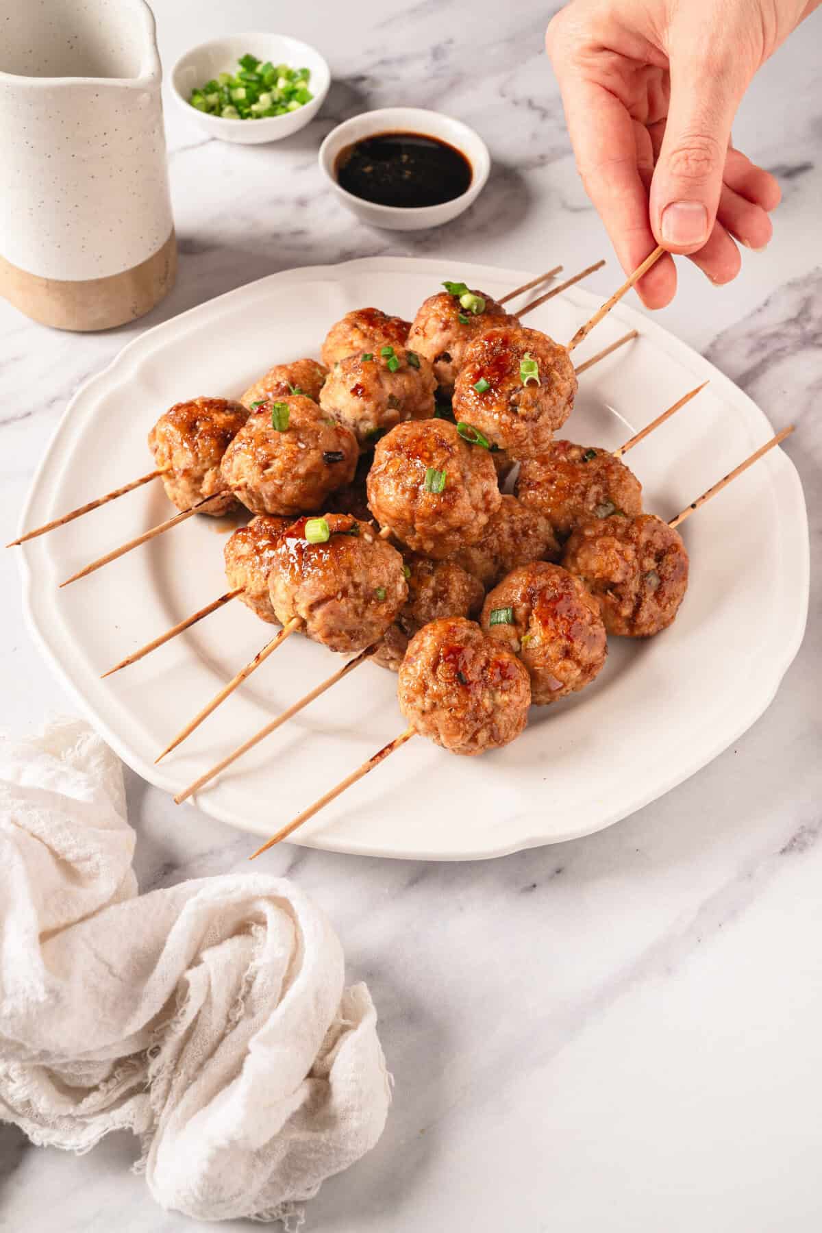 Skewered homemade meatballs on a white plate with dipping sauces and garnished with chopped green onions, perfect for healthy eating and meal prep.