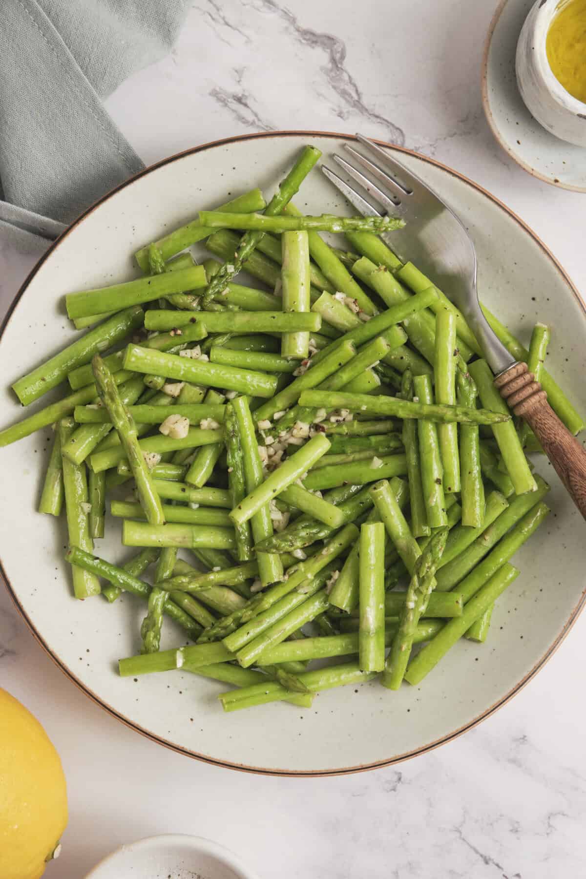 Steamed fresh asparagus spears garnished with garlic in a white bowl, healthy and nutritious vegetable side dish for a balanced diet.