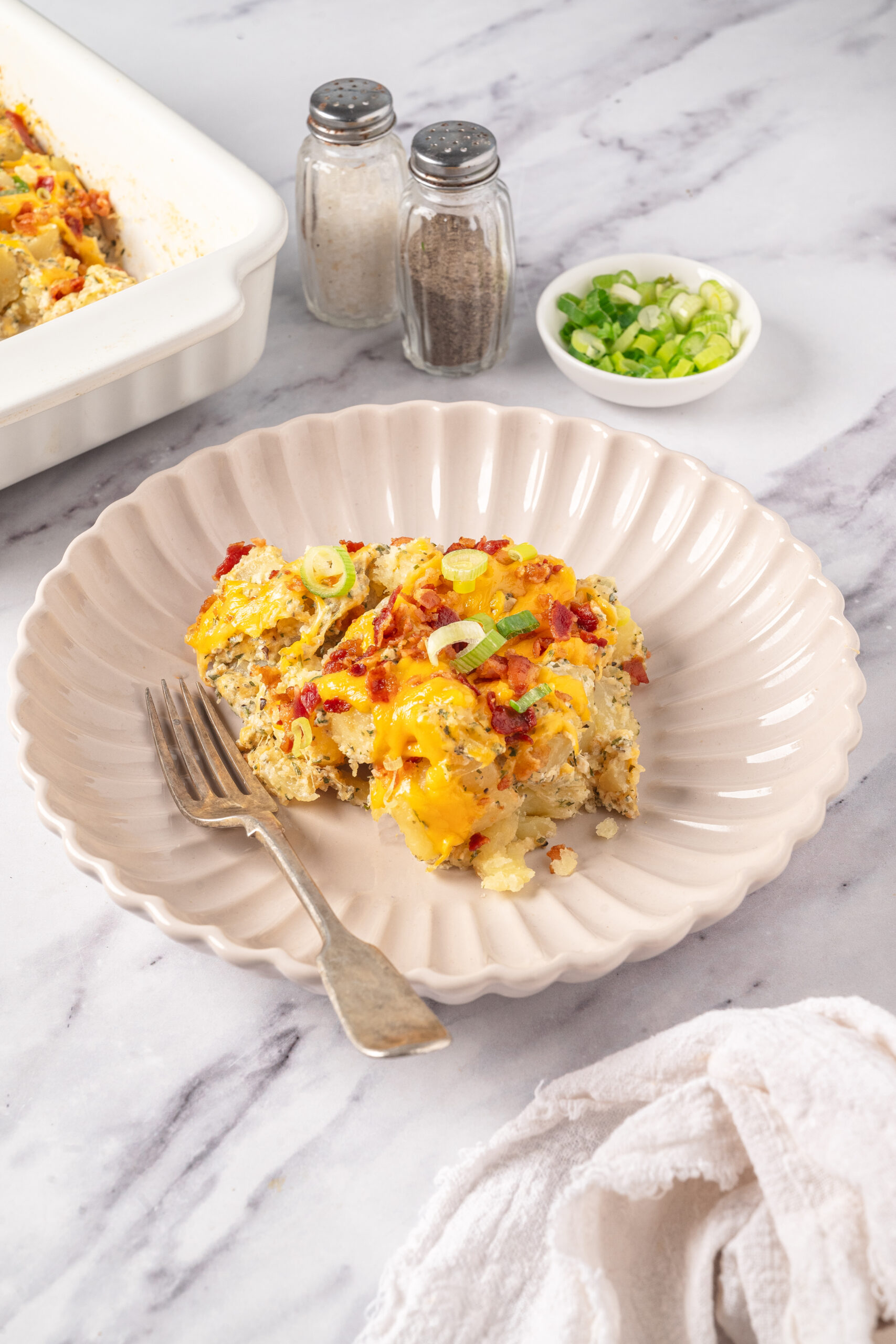 Baked breakfast casserole with cheese, bacon, and green onions on a beige plate.