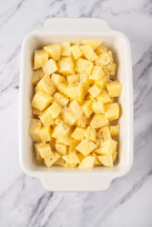 Tossing cubed Crack Potatoes with pepper in a baking dish.