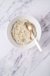 Creamy homemade ranch dip with herbs and shredded cheese in a white bowl on marble surface. Perfect for healthy snacking, party dips, or flavorful appetizers.