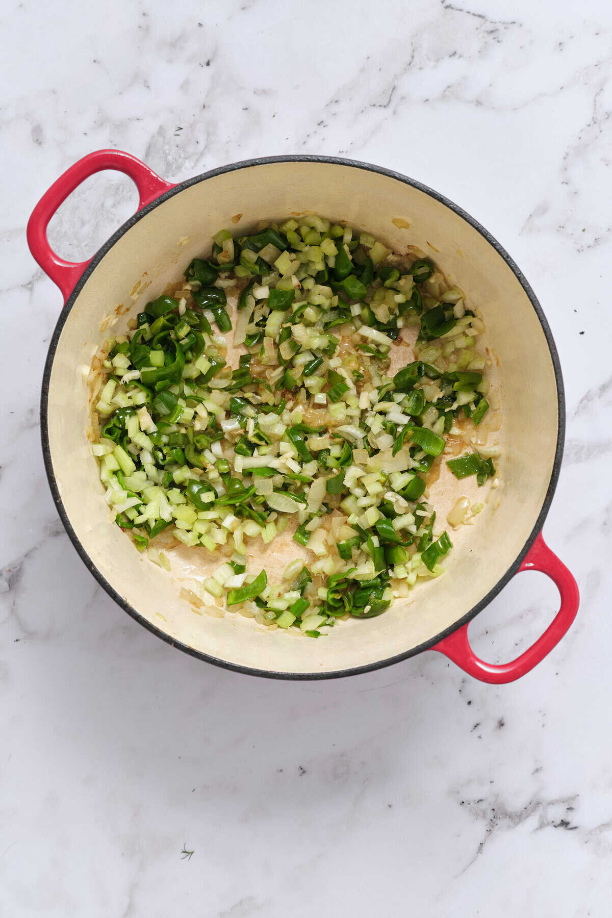 Diced green onions and leeks sautéing in a beige skillet with red handles, perfect for healthy recipes and meal prep.