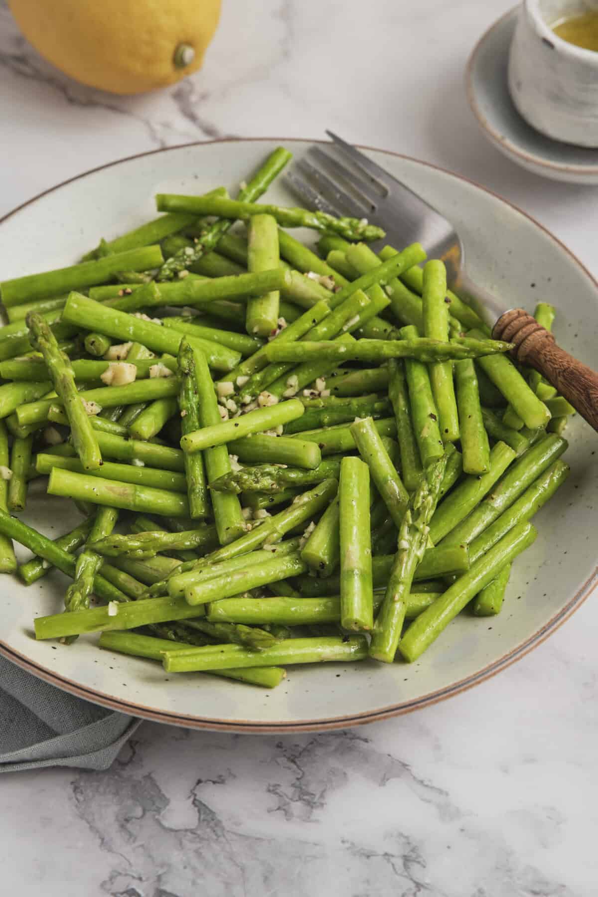 Steamed asparagus spears garnished with garlic on a white plate, healthy vegetable side dish for nutritious eating.