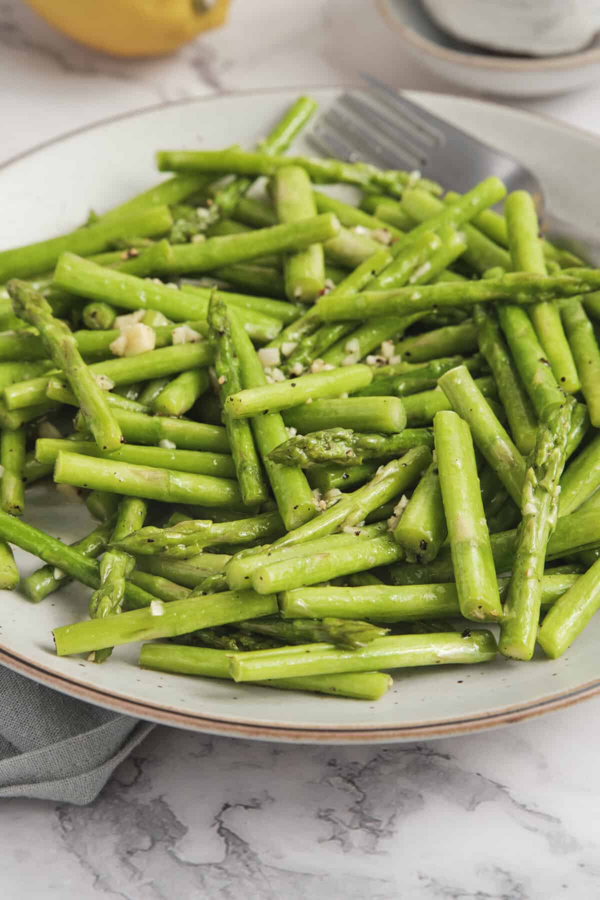 Steamed asparagus spears garnished with garlic and black pepper, served on a white plate for a healthy, low-calorie vegetable dish.