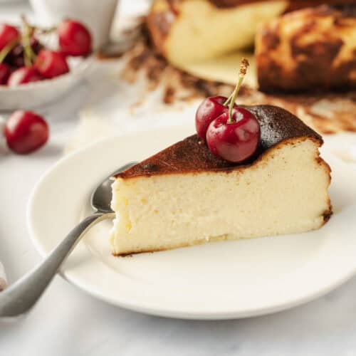 Cream cheese cheesecake topped with fresh cherries on a white plate with a silver fork, showcasing a delicious and healthy dessert recipe from Food Faith Fitness.