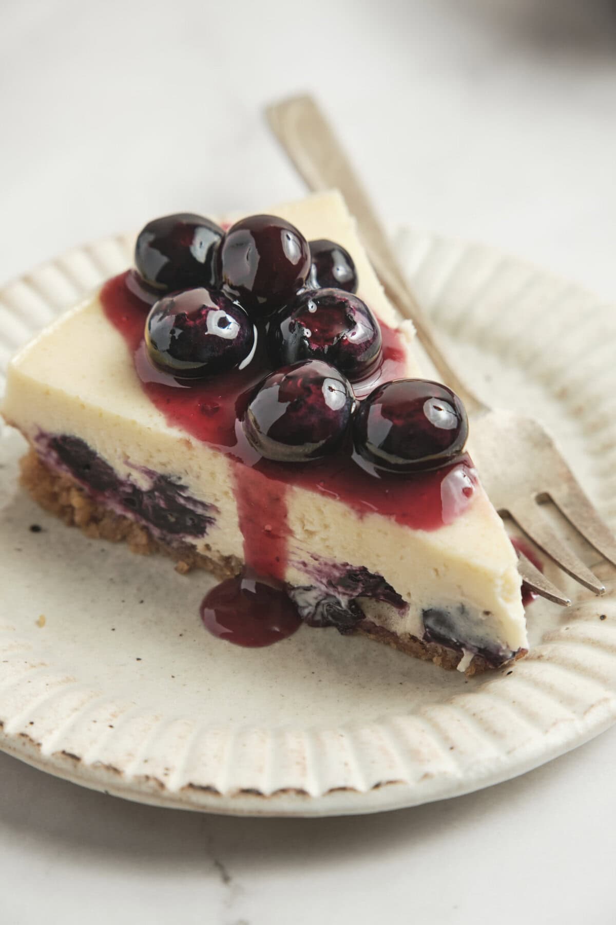 Fresh blueberry cheesecake with creamy filling, graham cracker crust, and blueberry topping on a white plate. Perfect for healthy dessert recipes and indulging guilt-free.
