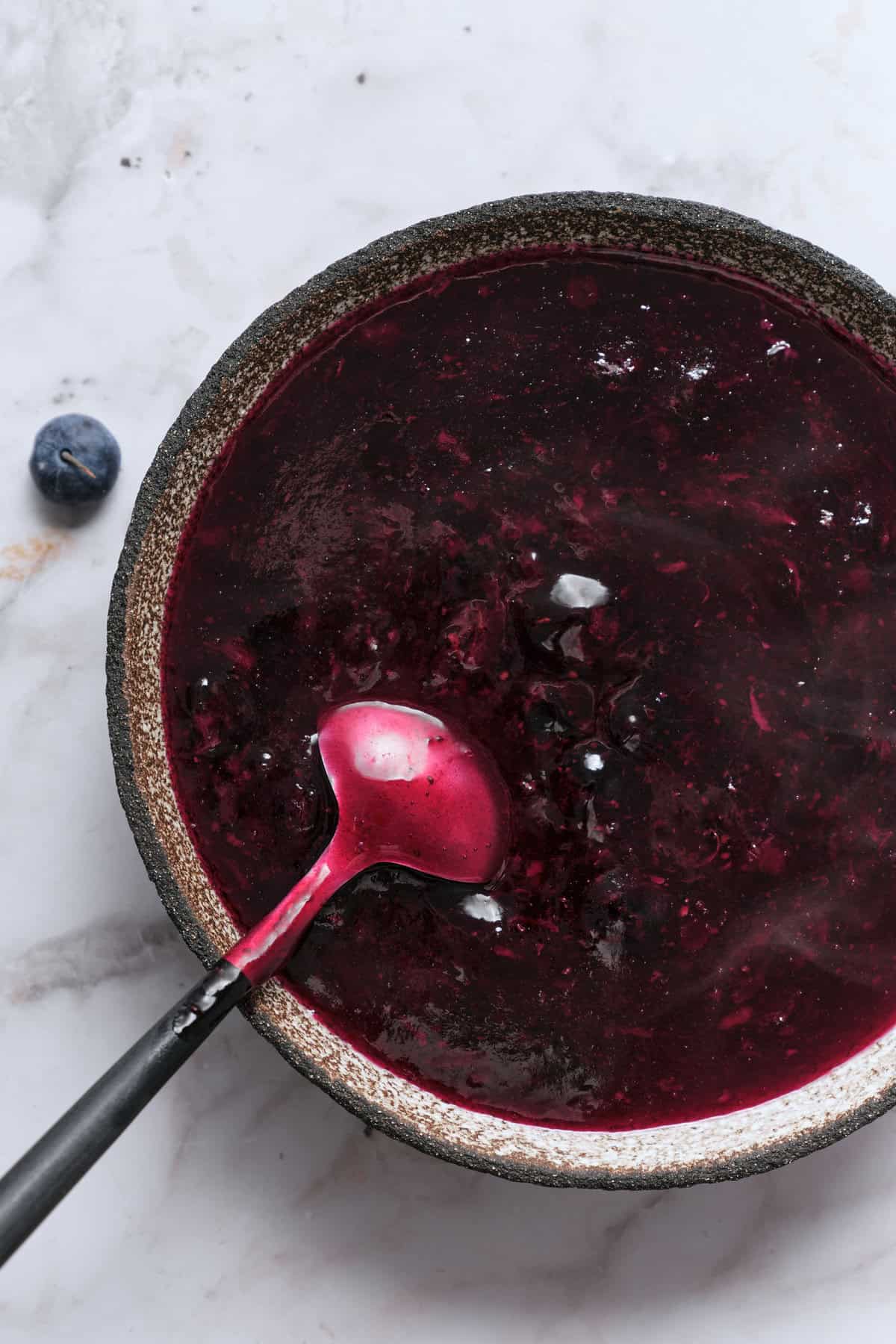Homemade blueberry jam in a rustic bowl with a spoon on a white marble surface for healthy eating and nutritious recipes.