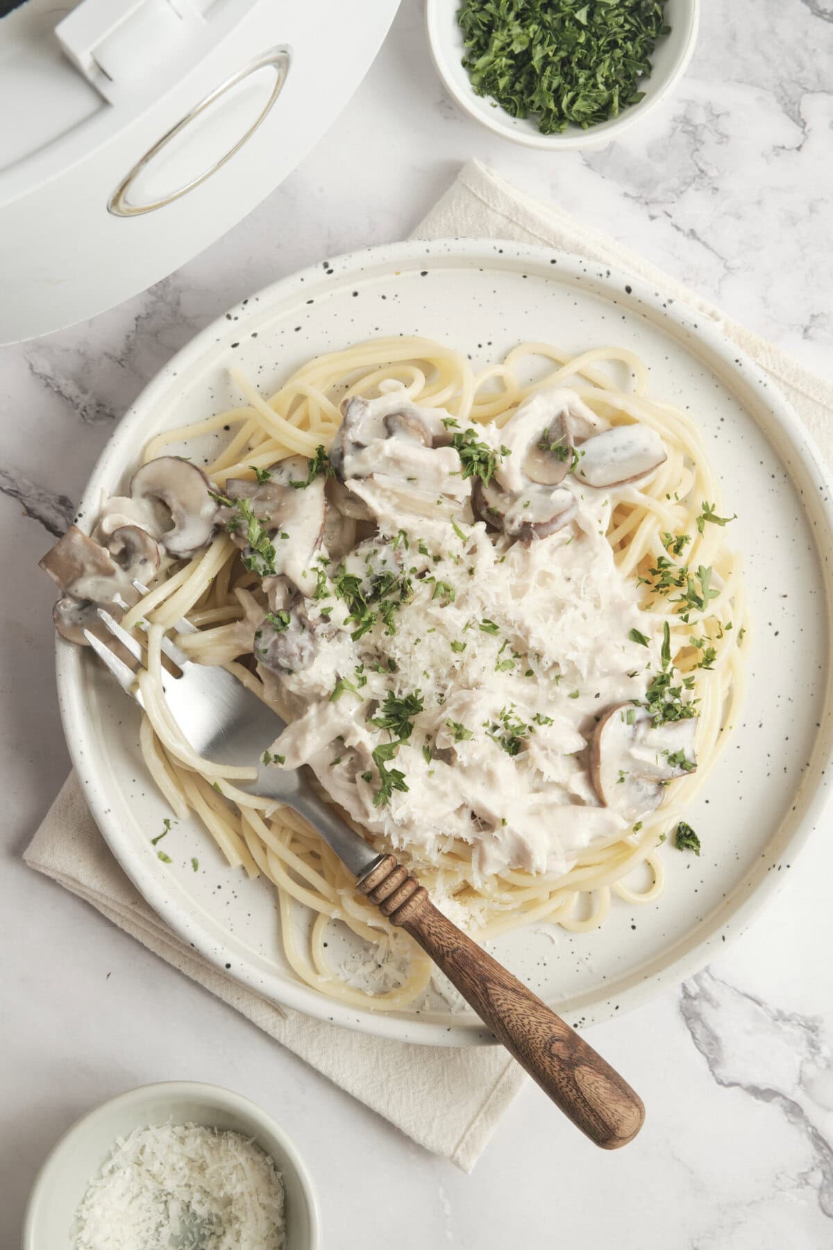 Creamy mushroom chicken alfredo pasta served on a white speckled plate with fresh parsley garnish. A light, healthy, and delicious meal perfect for food lovers and fitness enthusiasts.
