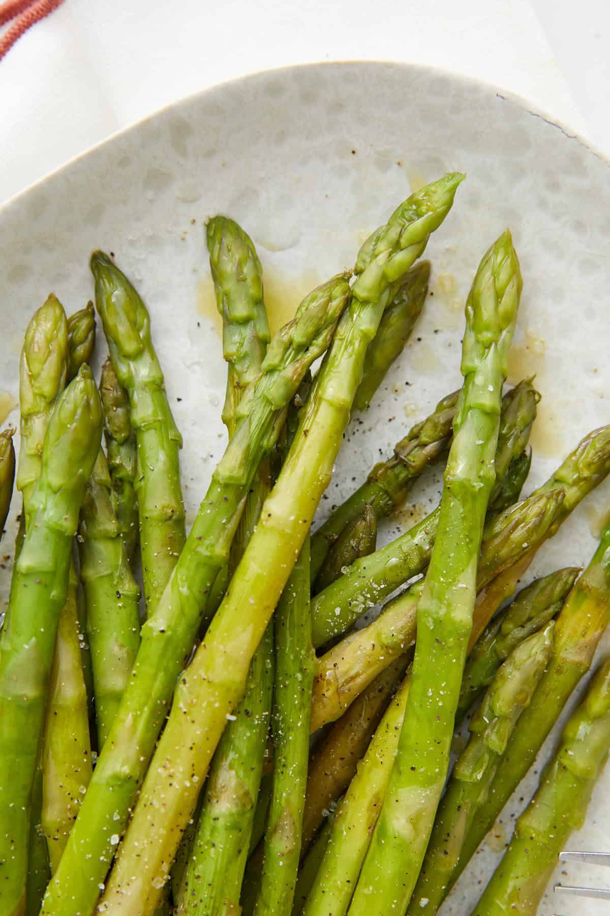 Fresh roasted asparagus spears drizzled with olive oil, seasoned with salt and pepper, on a white plate. A nutritious, healthy vegetable side dish perfect for balanced eating and fitness-focused meals.