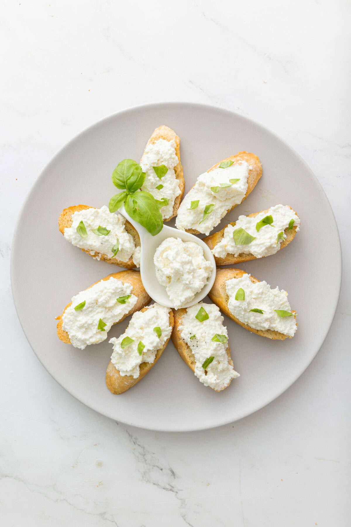 Cream cheese basil crostini appetizer, served on a white plate with fresh basil garnish, perfect for healthy snacks or party appetizers.