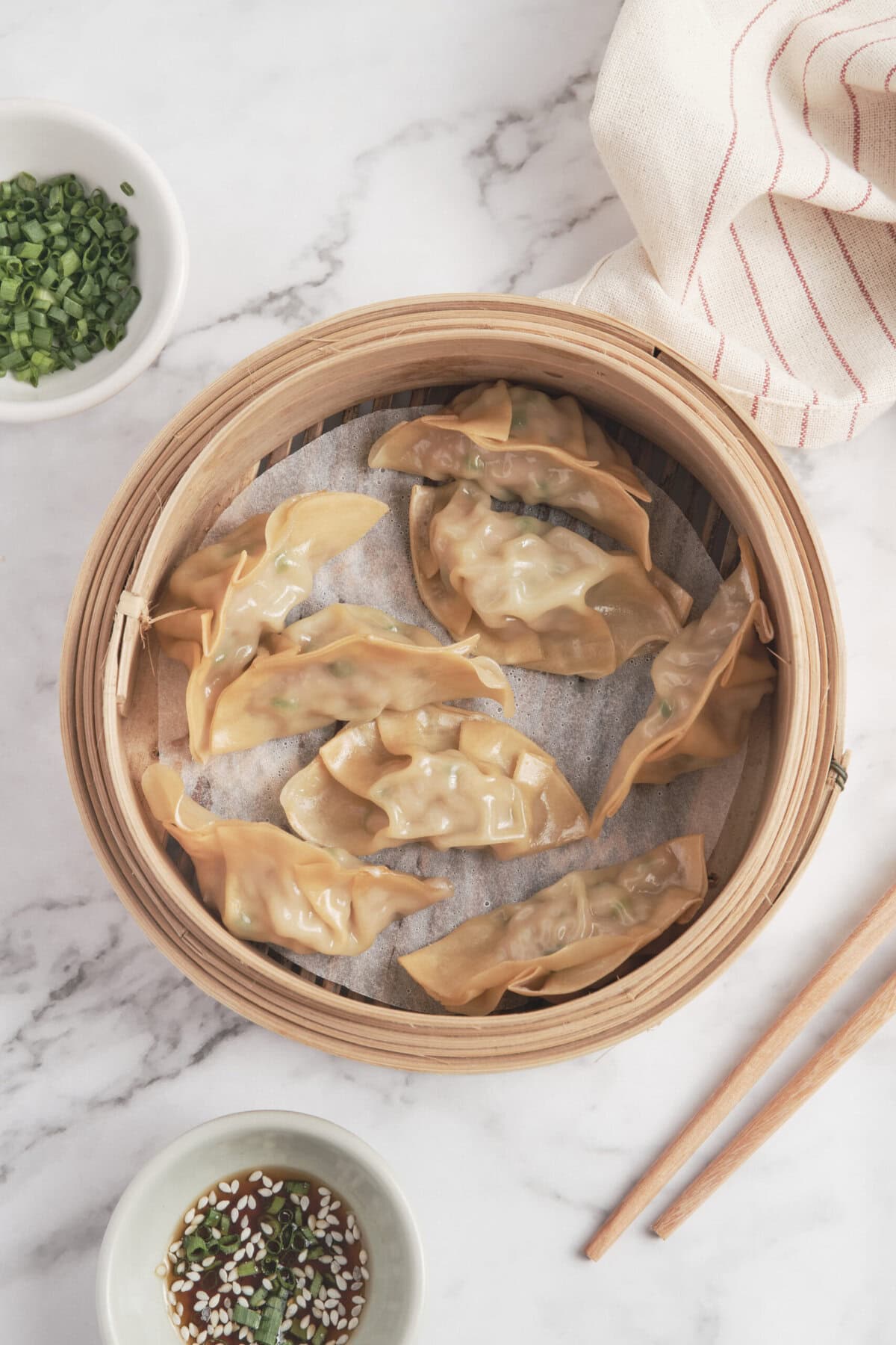 Steamed vegetable and chicken dumplings in bamboo steamer on marble surface with soy sauce dipping bowl and green onion garnish. Healthy Asian cuisine recipe for nutritious meals.