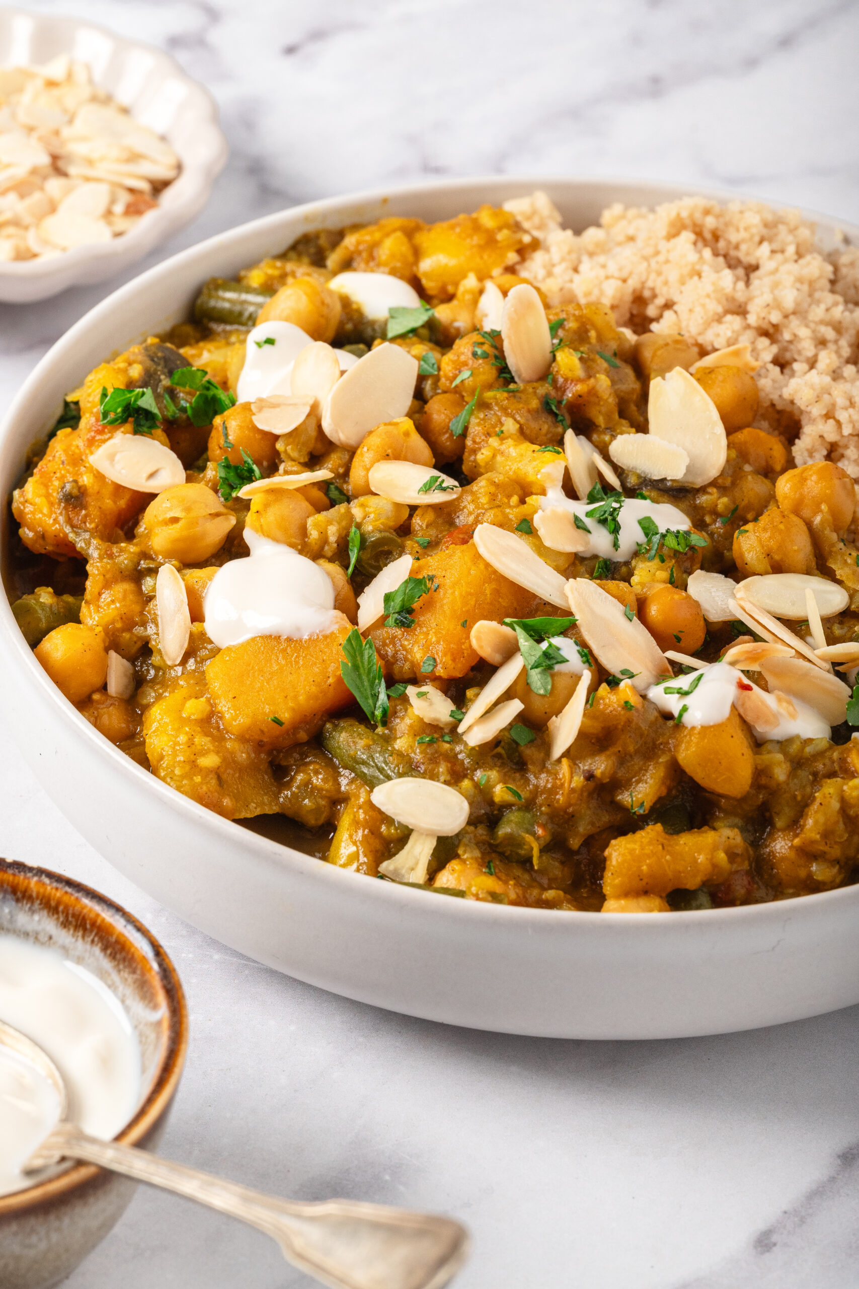 Savory chickpea and vegetable curry garnished with sliced almonds and fresh herbs, served alongside fluffy couscous, perfect for healthy, plant-based meal recipes.