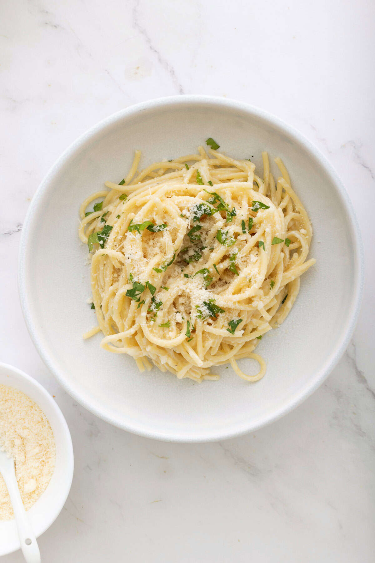 Creamy garlic pasta with parmesan cheese and fresh parsley on a white plate, healthy comfort food, easy vegan dinner, food recipe, gluten-free pasta.