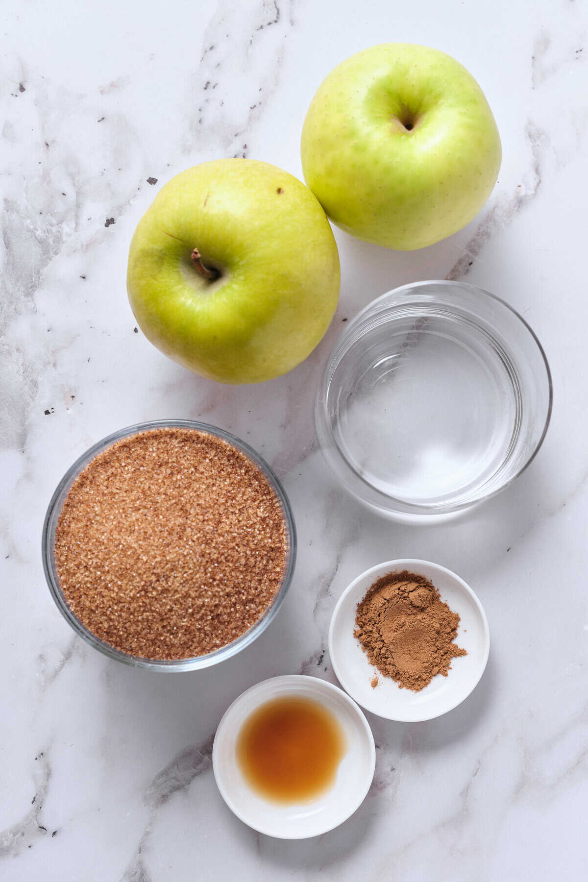 Fresh green apples, brown sugar, cinnamon, water and honey ingredients for healthy apple recipes on a white marble background.