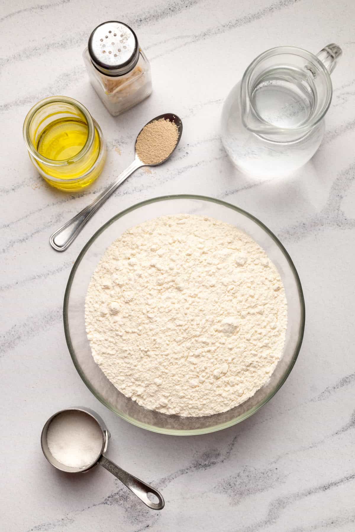 Flour, oil, salt, and baking ingredients for healthy baking recipes on a white marble surface.