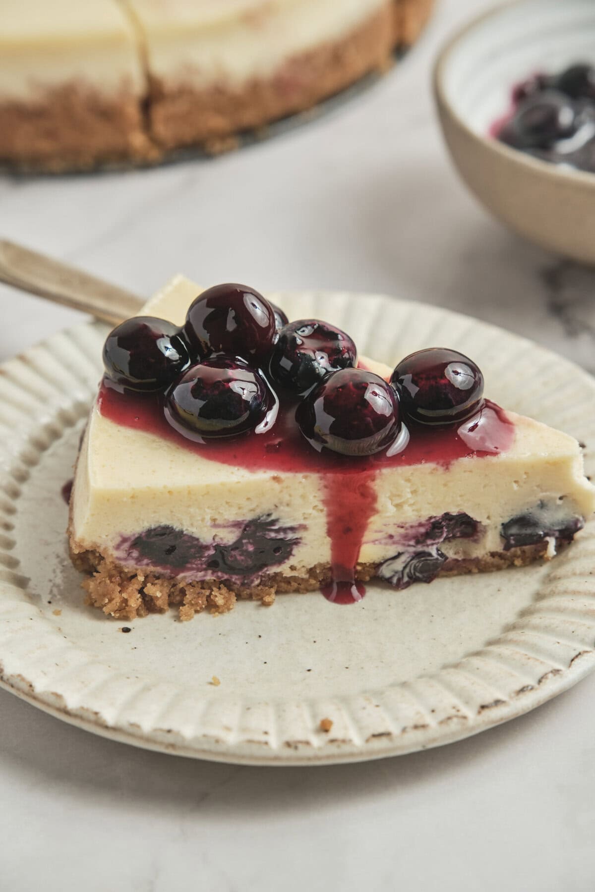 Creamy blueberry cheesecake topped with fresh blueberries and blueberry sauce on a white plate. Perfect for healthy dessert recipes and guilt-free treats.
