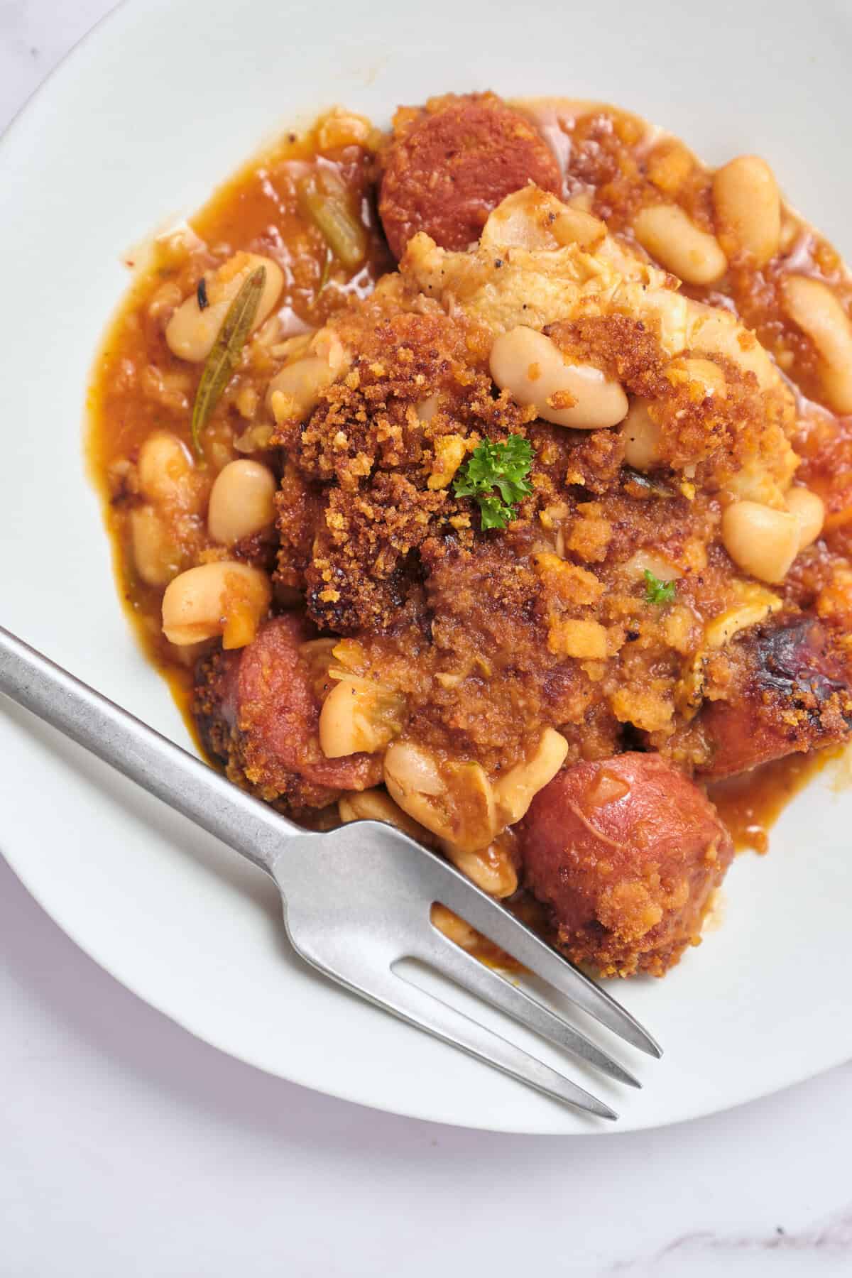 Creamy baked pasta with ground meat, beans, and tomato sauce in a white bowl on a silver fork.